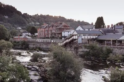 a town with a train station next to a river at Charming Eco Hideaway on the Dee River with Private Relaxing Hot Tub in Llangollen