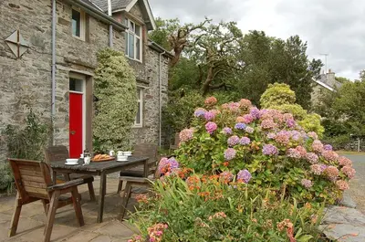 a table and chairs in front of a house with flowers at Fegla Fawr - Rustic, rural farmhouse near Barmouth in Arthog