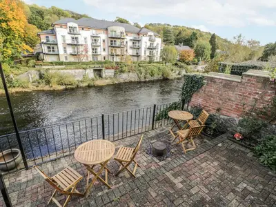 a patio with tables and chairs next to a river at Bryn Dwr in Llangollen