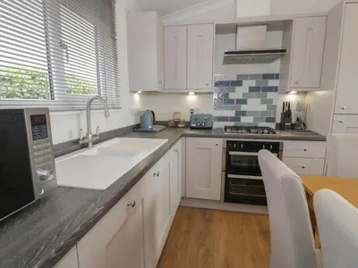 a kitchen with white cabinets and a sink and a table at Platinum Lodge 503 in Talybont