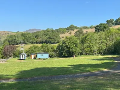a large grass field with a building in the distance at Tower Farm Holidays - Shepherd's Huts in Llangollen