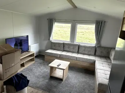 a living room with a couch and a tv at Luxury static caravan on SunnySands with mountain views in Barmouth