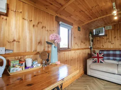 a room with a wooden wall with a table and a couch at Sharon's Shepherd Hut in Oswestry