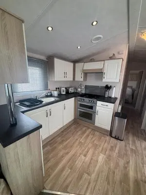 a kitchen with white cabinets and a wooden floor at T&J Seaview at Pengarreg in Llanrhystyd