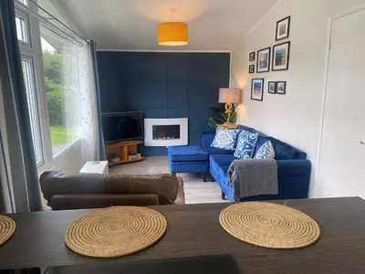 a living room with a blue couch and a tv at Chalet 8 Erw Porthor Happy valley in Tywyn