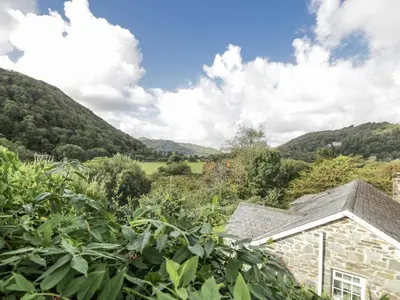 a view of a stone house with mountains in the background at Old Post Office in Maentwrog