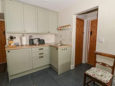 a kitchen with white cabinets and a sink and a chair at Llainorfa in New Quay