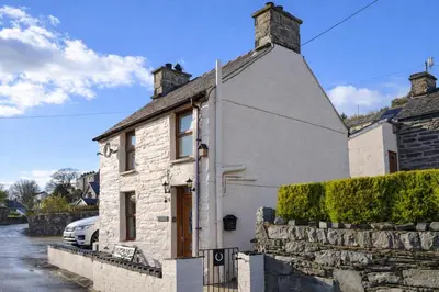 a white stone house with a car parked outside at Arddwyn - Cosy Welsh cottage in Penrhyndeudreath