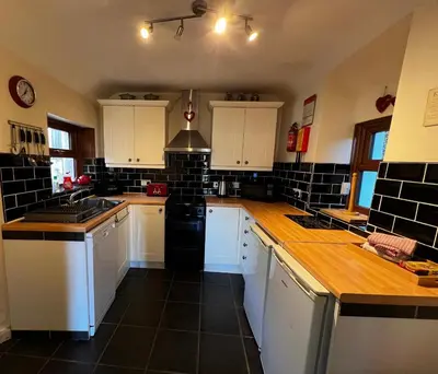 a large kitchen with white cabinets and black tiles at Arddwyn - Cosy Welsh cottage in Penrhyndeudreath