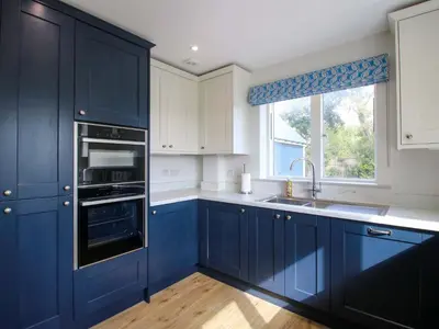 a blue kitchen with white cabinets and a window at Hoddell Pitch Cottage in Presteigne