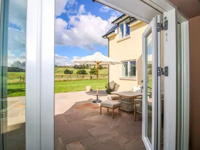 an open door to a patio with an umbrella at Hoddell Pitch Cottage in Presteigne