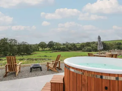 a hot tub on a patio with chairs and a grill at Yr Awen - Inspiration in Lampeter