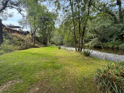 a grassy field next to a river with trees at The Owl's Nest - Uk50546 in Machynlleth