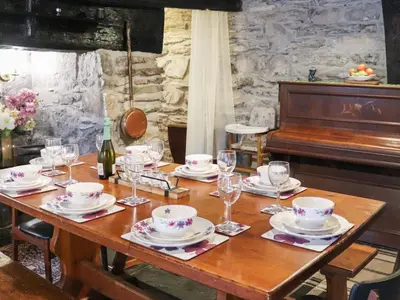 a wooden table with plates and glasses and a piano at Cynfal Fawr Farmhouse in Ffestiniog