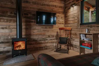 a living room with a woodburning stove and a chair at Woolly Wood Cabins - Nant in Abbey-Cwmhir
