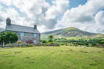 a stone house in a field with mountains in the background at Pwll-Y-March in Llanbedr
