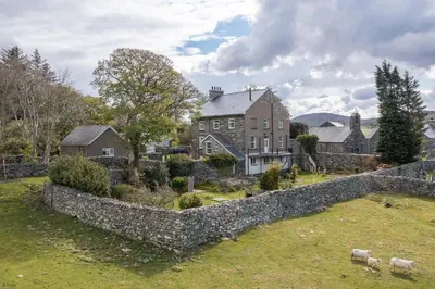 a large house with a stone wall and sheep in a yard at Rheithordy in Blaenau-Ffestiniog