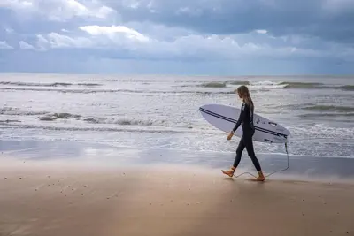 a woman walking on the beach with a surfboard at Stabl-Bennar in Dyffryn
