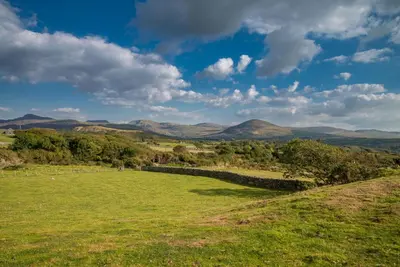 a field with a fence and mountains in the background at Maes-Artro-Lodge in Llanbedr