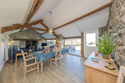 a dining room and living room with a stone wall at Bwthyn-Bennar in Dyffryn
