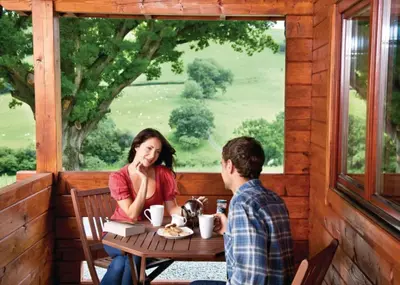 a man and a woman sitting at a table on a porch at Trewythen Lodges in Towyn