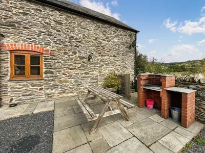 a wooden bench on a patio in front of a stone building at Granary - Uk50617 in Corwen