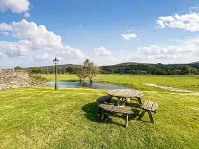 a picnic table and bench in a field with a pond at Granary - Uk50617 in Corwen