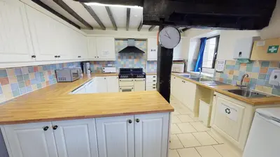 a kitchen with white cabinets and a clock on the wall at Traditional Welsh Longbarn in Aber-Brân