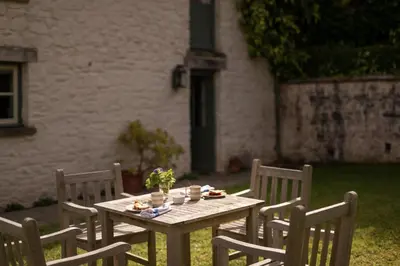 a wooden table with three chairs and a table with food on it at West Cottage in Llandovery