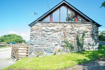 a stone building with a window and a wooden fence at Beudy-Talsarnau in Talsarnau