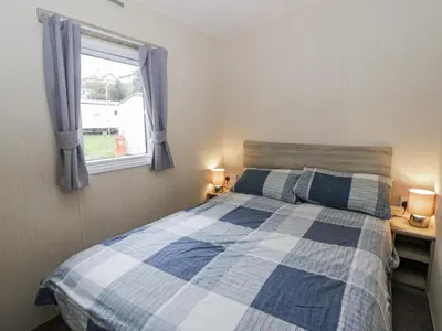 a bedroom with a blue and white bed and a window at Brynowen Holiday Park - 22432 in Borth