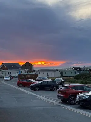 a parking lot with cars parked in front of a sunset at Welsh Seaview Stay 3 bed caravan by pool, club and beach in Aberystwyth