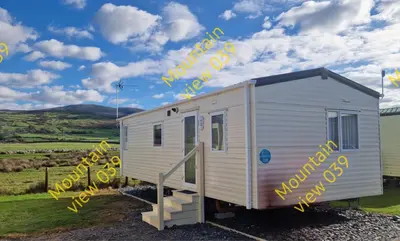 a white tiny house with yellow letters on it at Mountain view 039 in Barmouth