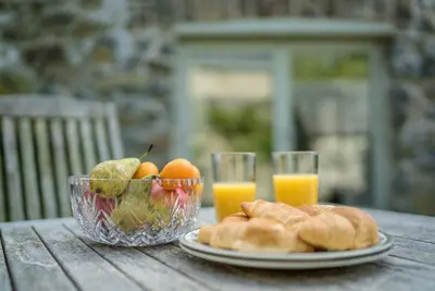 a table with a bowl of fruit and two glasses of orange juice at Coed-Stable in Dolgellau