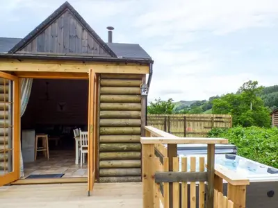 a wooden cabin with a deck and a table at Deer Cabin-hot tub-dog friendly-mountain view in Llanbrynmair