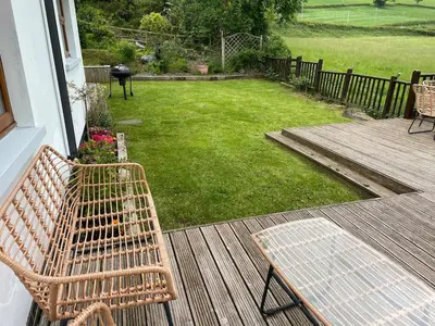 a wicker bench sitting on a porch with a yard at Swn yr Coed in Sennybridge