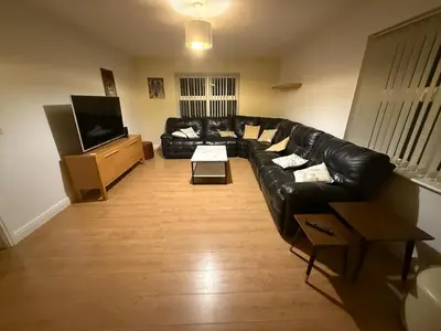 a living room with a black leather couch and a television at Swn yr Coed in Sennybridge