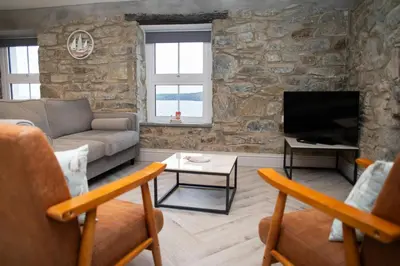 a living room with a stone wall with a couch and a tv at Bay View New Quay in New Quay