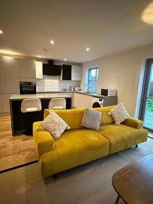 a living room with a yellow couch and a kitchen at Woodland View House in Norton Canon