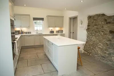 a kitchen with white cabinets and a stone wall at Gelli Genlas Aberaeron in Llanarth