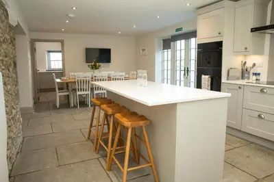 a kitchen with a white counter and wooden stools at Gelli Genlas Aberaeron in Llanarth
