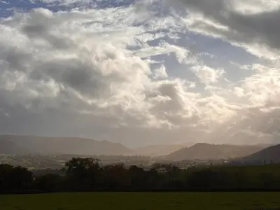 a cloudy sky with a green field and mountains at Nant Hafren Retreat in Llanwnog