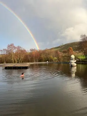 a person swimming in a pond with a rainbow at The Granary - Wild Swimming, Sauna, Peace & Quiet, Nr Bala in Corwen