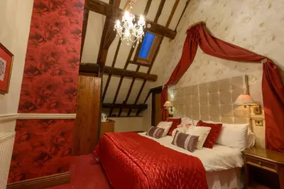 a bedroom with a bed with red sheets and a chandelier at Mortimers Cross Guest House in Mortimer's Cross