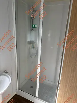 a shower with a glass door next to a sink at Snowdon Summit 002 in Barmouth