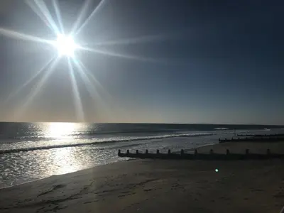 a sun shining over the ocean on a beach at The Woodlands Caravan in Bryn-glâs Station