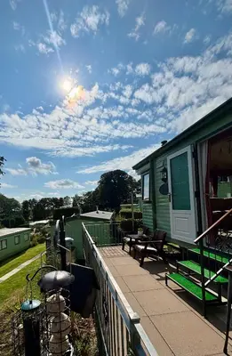 a green rv on a deck with a table and benches at The Woodlands Caravan in Bryn-glâs Station