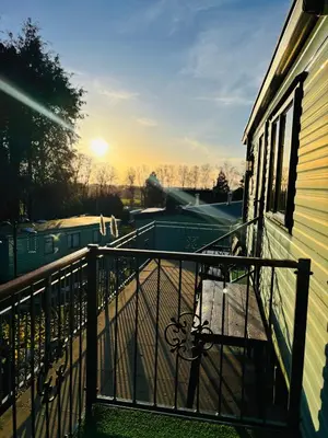 a balcony of a house with the sunset in the background at The Woodlands Caravan in Bryn-glâs Station