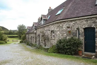 a stone house with a blue door and a gravel driveway at Abbey Cottages- Red Kite Lodge in Talley