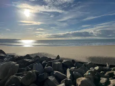 a beach with rocks and the sun in the sky at Dolphin View in Llanddwywe